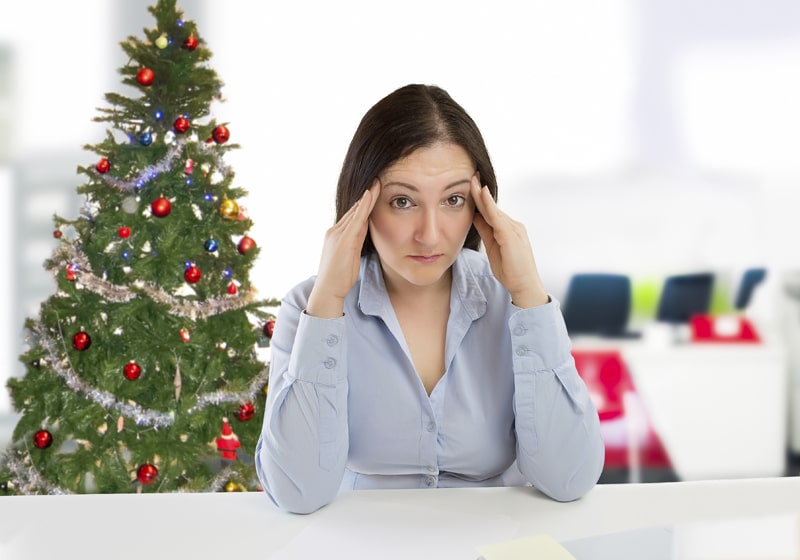 Woman holding her head while sitting in the office during the holidays