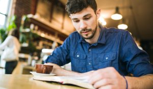 A man concentrates with a serious face as he reads the Bible or a book in his favorite coffee shop